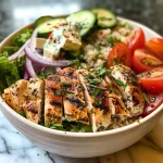 A side view of a Greek Chicken Bowl showcasing layers of chicken, veggies, and creamy tzatziki sauce.