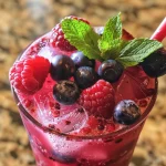 Glass of sparkling lemonade filled with colorful mixed berries, appearing cool and inviting.