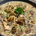 A warm bowl of creamy wild rice chicken soup, showcasing a mix of rice, chicken, and greens.