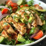 A fresh chicken salad displaying mixed greens, avocado, and sliced vegetables.