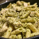 Juicy chicken breasts mixed with fettuccine and creamy pesto in a vibrant dish.