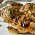 Side view of tender grilled chicken topped with a honey mustard sauce, resting on a plate.