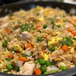 Side view of a serving of chicken fried rice topped with sesame seeds and onions.