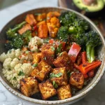 A side view of a nutritious quinoa bowl filled with spiced tofu and assorted roasted vegetables.