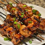 Side view of succulent chicken skewers, marinated in Teriyaki sauce and topped with herbs.