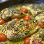 Close-up of creamy pesto chicken served with roasted tomatoes and fresh spinach.
