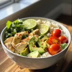 A delicious bowl of creamy avocado chicken served over rice, with colorful cherry tomatoes and optional toppings.