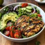 A close-up view of a grilled chicken avocado salad bowl, showcasing vibrant greens and sliced avocado.