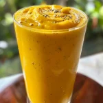 A close-up view of a vibrant mango peach smoothie in a glass, showcasing its creamy texture.