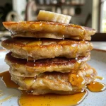 Close-up view of golden-brown oatmeal banana hotcakes stacked on a plate.