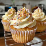 Side view of a moist vanilla cupcake topped with creamy frosting and sprinkles.