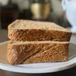 Close-up of a slice of whole wheat sourdough sandwich bread on a wooden cutting board.