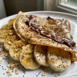 Close-up of a plate of Almond Oat Banana Crepes topped with sliced bananas and melted chocolate.