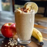 Close-up view of a creamy apple cinnamon smoothie in a glass, garnished with a slice of apple.