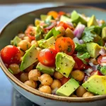 A colorful salad featuring diced avocados, chickpeas, halved cherry tomatoes, and red onion.