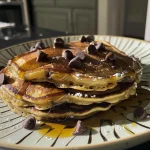 Close-up of golden banana chocolate chip pancakes stacked on a plate.