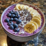 Close-up view of a vibrant Blueberry Coconut Smoothie Bowl topped with chia seeds, nuts, and fresh blueberries.