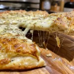Close-up of a cheesy flatbread overflowing with melted mozzarella.