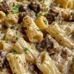 Close-up view of creamy garlic beef pasta with rigatoni and parsley garnish.