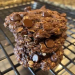 A side view close-up of a stack of double chocolate oatmeal cookies on a wooden surface.
