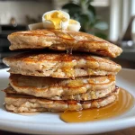 Fluffy protein pancakes stacked on a plate, drizzled with syrup.