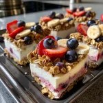 Close-up of frozen yogurt bites topped with granola and fresh fruit in a muffin pan.