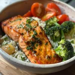 A close-up view of a Garlic Butter Salmon Bowl featuring salmon fillets, rice, broccoli, and cherry tomatoes.