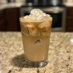 Close-up side view of a glass filled with an Iced Vanilla Latte, featuring creamy milk and ice.