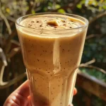 A vibrant peach banana protein smoothie in a clear glass with a straw.