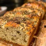 A close-up side view of a Rustic Rosemary Olive Loaf with a golden brown crust and visible black olives.