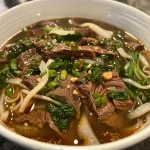 Close-up view of a steaming bowl of Spicy Beef Noodle Soup with visible beef slices and noodles.