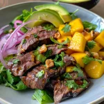 Close-up view of a vibrant steak and mango salad featuring sliced steak, mango, avocado, and fresh greens.