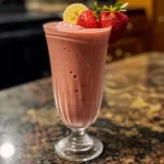 Close-up view of a vibrant strawberry banana smoothie in a glass with fresh strawberries nearby.