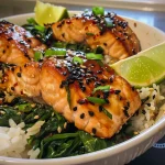A close-up view of a bowl featuring salmon, spinach, and rice, garnished with sesame seeds.
