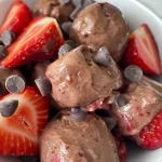 A close-up view of chocolate strawberry frozen yogurt bites, showcasing their glossy dark chocolate coating and visible strawberry pieces.