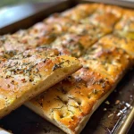 Close-up view of a golden-brown whole wheat herb focaccia bread with fresh basil.