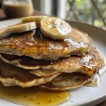 Close-up of golden brown banana protein pancakes stacked on a plate with a soft texture.