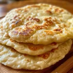 Close-up side view of golden-brown yogurt flatbreads stacked on a wooden surface.
