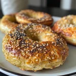 ['Close-up view of golden brown air fryer protein bagels topped with sesame seeds.', 'Side angle of fluffy air fryer protein bagels garnished with poppy seeds and everything seasoning.', 'Detailed image of sliced air fryer protein bagels showcasing their soft texture and toppings.', 'Close-up perspective of protein bagels freshly made in an air fryer, displaying a crispy exterior.']