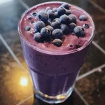 ['Close-up view of a creamy blueberry protein smoothie in a glass, showcasing its rich purple color.', 'Side view of a thick blueberry smoothie topped with yogurt, garnished with fresh blueberries.', 'A vibrant blueberry smoothie in a clear glass with a straw, highlighting its frosty texture.', 'Delicious blueberry protein smoothie in a side profile, featuring layers of yogurt and fruit.']