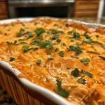['Close-up view of a creamy Buffalo Chicken Dip in a serving dish, garnished with a sprinkle of cheese.', 'Side perspective of a bowl filled with high-protein Buffalo Chicken Dip, showcasing its rich texture and color.', 'Juicy Buffalo Chicken Dip in a white bowl, with melted cheese on top, ready for serving.', 'High-protein Buffalo Chicken Dip displayed with a spoon, highlighting its smooth consistency and vibrant color.']