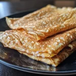 ['A close-up of a stack of high protein crepes topped with fresh berries.', 'Side view of golden-brown high protein crepes served on a plate with syrup.', 'Juicy, folded high protein crepes filled with a creamy filling, displayed on a wooden table.', 'A vibrant arrangement of high protein crepes garnished with honey and fruits.']