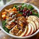 ['A close-up view of a Maple Dijon Fall Harvest Power Bowl featuring colorful ingredients like quinoa, sliced apple, sweet potato, and kale.', 'Side view of a vibrant Power Bowl with chicken, roasted pecans, dried cranberries, and a drizzle of Maple Dijon dressing.', 'A detailed image showing a nutritious bowl filled with quinoa, kale, sweet potato, apple slices, and toppings.', 'An appetizing close-up of a fall-inspired dish highlighting maple dressing over chicken and various fresh ingredients.']