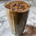 ['A close-up view of a mint chocolate green protein smoothie in a glass, showcasing its rich green and brown colors.', 'Side view of a smoothie made with spinach, chocolate protein powder, and mint, garnished with mint leaves.', 'Refreshing mint chocolate protein smoothie in a clear glass, highlighting the creamy texture and vibrant green color.', 'A delicious mint chocolate smoothie featuring spinach and banana, captured in a close-up shot.']