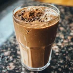 ['Close-up view of a creamy mocha protein shake in a glass with a straw.', 'Side angle shot of a delicious mocha protein shake topped with cocoa powder and a banana slice.', 'Close-up of a mocha protein shake, highlighting its rich texture and color in a well-lit setting.', 'A side view of a mocha protein shake with ingredients like cocoa and banana visibly blended.']