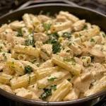 ['Close-up of a creamy One Pot Rigatoni Alfredo with Chicken, showcasing pasta, chicken pieces, and kale.', 'A side view of a delicious One Pot Rigatoni Alfredo with Chicken, featuring rigatoni and a rich sauce.', 'Juicy chicken and rigatoni in a rich Alfredo sauce, garnished with kale and Parmesan.', 'A vibrant dish of One Pot Rigatoni Alfredo with Chicken, highlighting the creamy texture and fresh ingredients.']