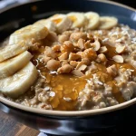 ['A close-up side view of a creamy bowl of Peanut Butter Banana Oatmeal topped with sliced bananas.', 'A vibrant bowl of oatmeal featuring peanut butter and banana slices, seen from the side.', 'A delicious serving of Peanut Butter Banana Oatmeal with a smooth texture and banana pieces on top.', 'A hearty bowl of oatmeal with peanut butter and mashed banana, captured in a close-up side angle.']