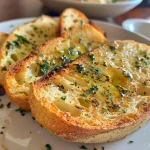 ['Close-up of crispy sourdough garlic toast, golden brown with melted herb butter.', 'Side view of juicy sourdough garlic toast topped with garlic herb butter on a plate.', 'Detailed view of toasted sourdough bread, glistening with melted garlic butter.', 'Appetizing shot of four slices of sourdough garlic toast, showing texture and toppings.']
