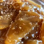 ['A close-up view of a jar filled with glossy apple cider caramel sauce.', 'Side view of delicious apple cider caramel sauce in a glass container, glistening in light.', 'A rich, amber-colored apple cider caramel sauce shown in a detailed close-up.', 'Close-up of thick apple cider caramel sauce drizzled in a clear bowl, highlighting its texture.']