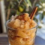 ['Close-up of a refreshing apple cider slushie with ice and cinnamon.', 'Side view of a frosty apple cider slushie in a glass with a cinnamon stick.', 'Delicious apple cider slushie showcasing a blend of spices on top of ice.', 'Ice-filled slushie glass filled with apple cider, garnished with a cinnamon stick.']